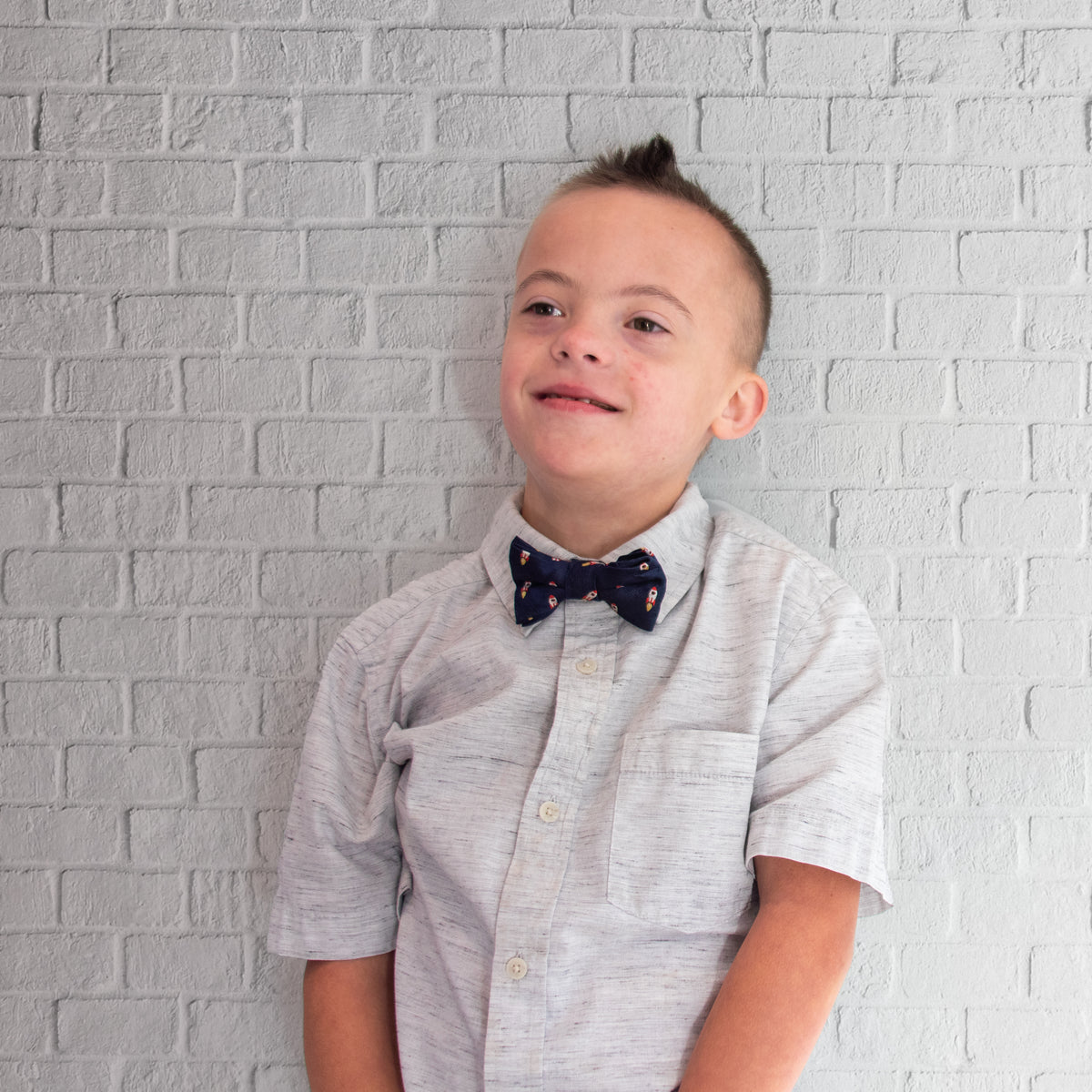 Bow wearing rock emoji bowtie in front of a white brick wall.